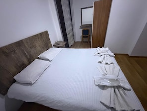 A room with a wooden headboard, a bed with white linens, a wooden floor, and a small table with a chair. - Kapadokya Pansiyon (Nevşehir)