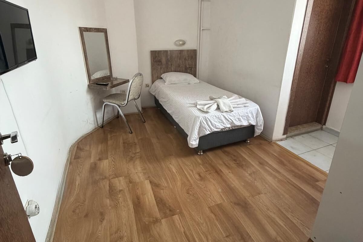 Un alojamiento pequeño de una sola habitación, con cama, escritorio con silla, espejo y televisión.