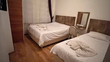 A hotel room with two beds, wooden flooring, a wooden wardrobe, a mirror, and a ceiling light fixture.