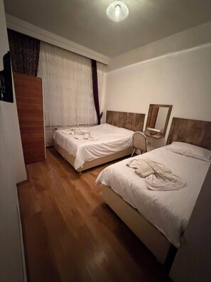 Habitación de hotel con dos camas, piso de madera, un armario de madera, un espejo y una lámpara en el techo.