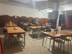 Un comedor con varias mesas y sillas, paneles de madera en las paredes y suelo de baldosas.