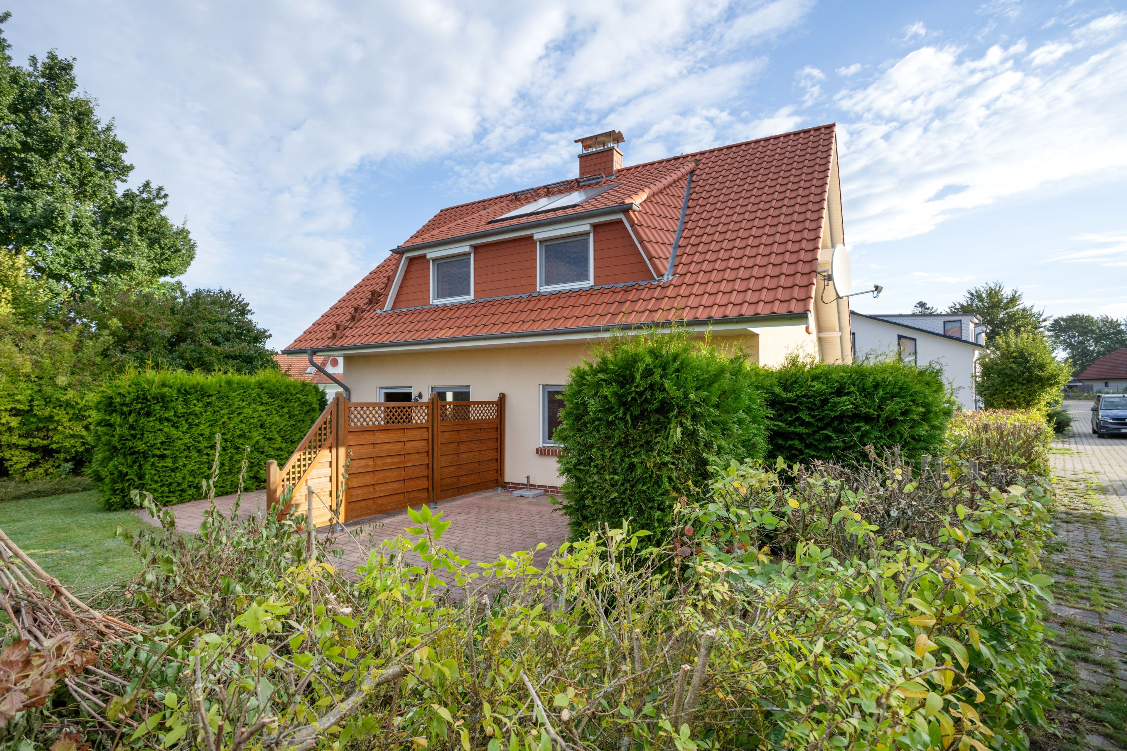 Ein zweistöckiges Haus mit rotem Ziegeldach, einem hölzernen Tor und einem gepflasterten Auffahrtsweg.