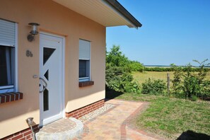 Una casa con puerta blanca, dos ventanas con contraventanas y un sendero de ladrillo que lleva a un patio cubierto de césped.