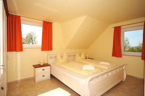 A bedroom with a single bed, a nightstand, a window with curtains, and a view of trees outside.