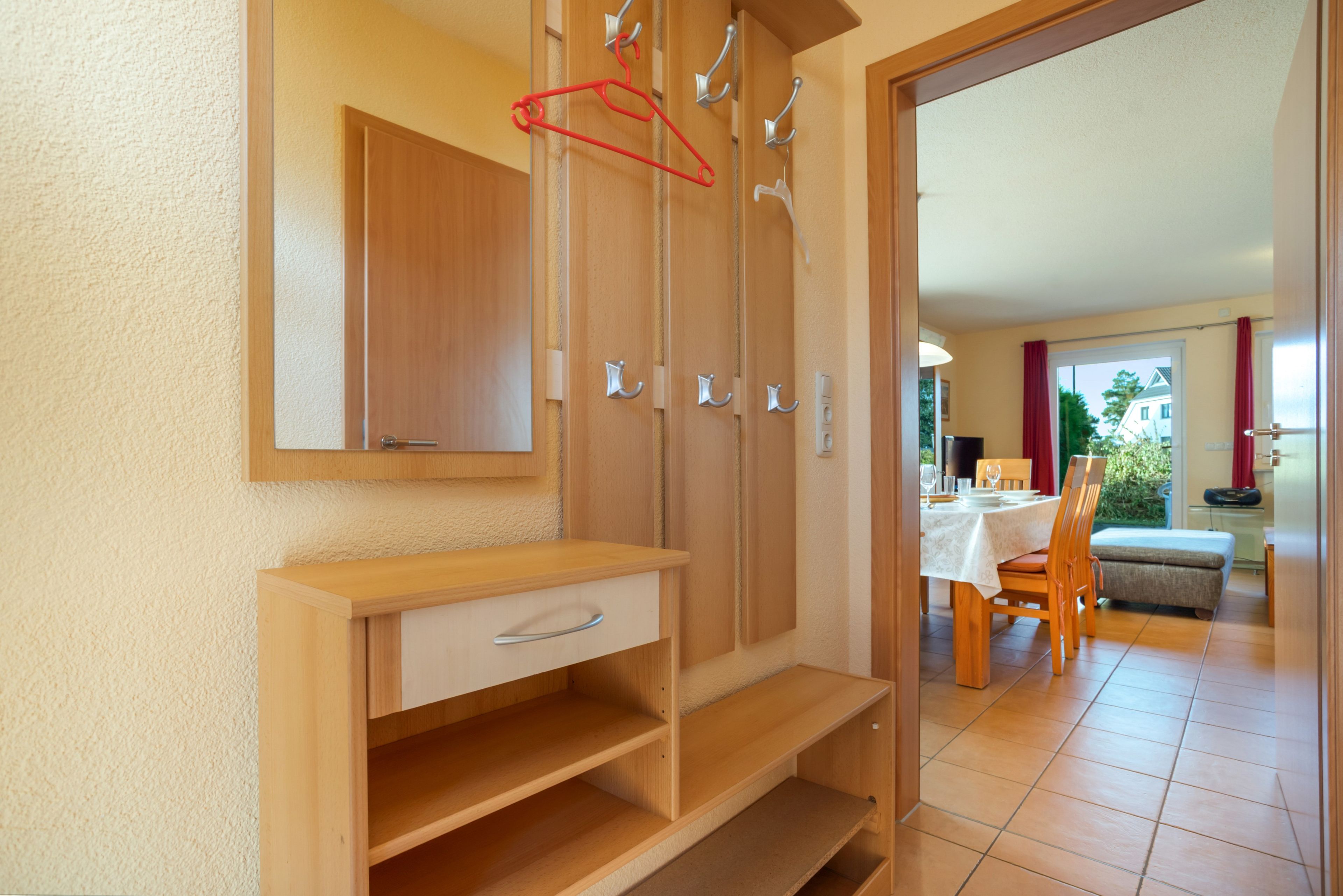 Ein Zimmer mit einem Holzschrank, einem Spiegel und einem Essbereich, der durch einen offenen Durchgang sichtbar ist.