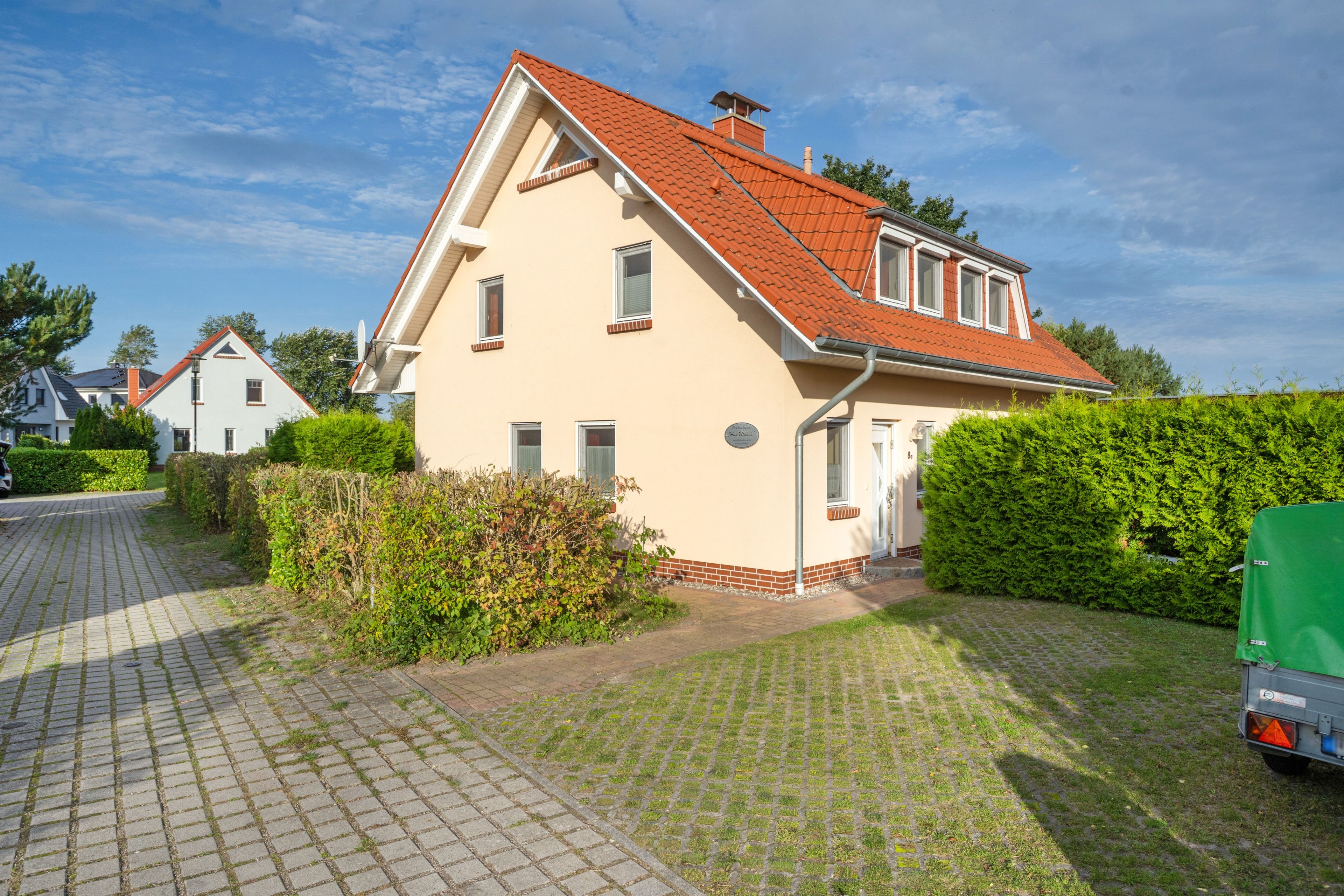 Ein zweigeschossiges Haus mit rotem Ziegeldach, einer Ziegelbasis und einem gepflasterten Einfahrt.