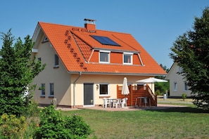 A two-story house with a sloped roof, a visible chimney, and a small patio area with a table and chairs.