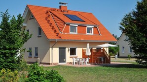 A two-story house with a sloped roof, a visible chimney, and a small patio area with outdoor furniture. - Hus Utblick in Fuhlendorf (Fuhlendorf)