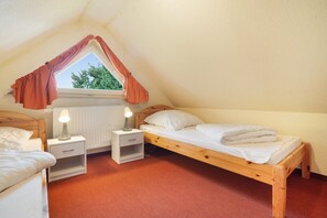 Une petite chambre à coucher accueillante, avec un plafond en pente, une fenêtre avec des rideaux, un lit, une table de chevet avec une lampe et un radiateur.
