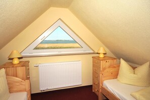Ein Schlafzimmer mit schrägen Wänden, einem Fenster mit Meerblick, einem Heizkörper, Holzmöbeln und zwei Nachttischlampen.