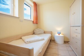 A small, single-bed room with a wooden headboard, a bedside lamp, and a wardrobe with multiple drawers. - Hus Utblick in Fuhlendorf (Fuhlendorf)