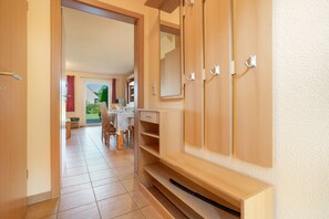 A hallway with a wooden wardrobe, a dining area with a table and chairs, and a view of a garden through an open door. - Hus Utblick in Fuhlendorf (Fuhlendorf)