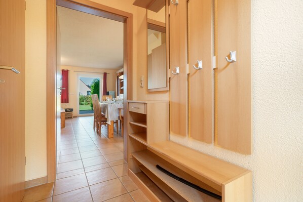 Un couloir avec une armoire en bois, un coin repas avec une table et des chaises, et une vue sur un jardin par une porte ouverte.