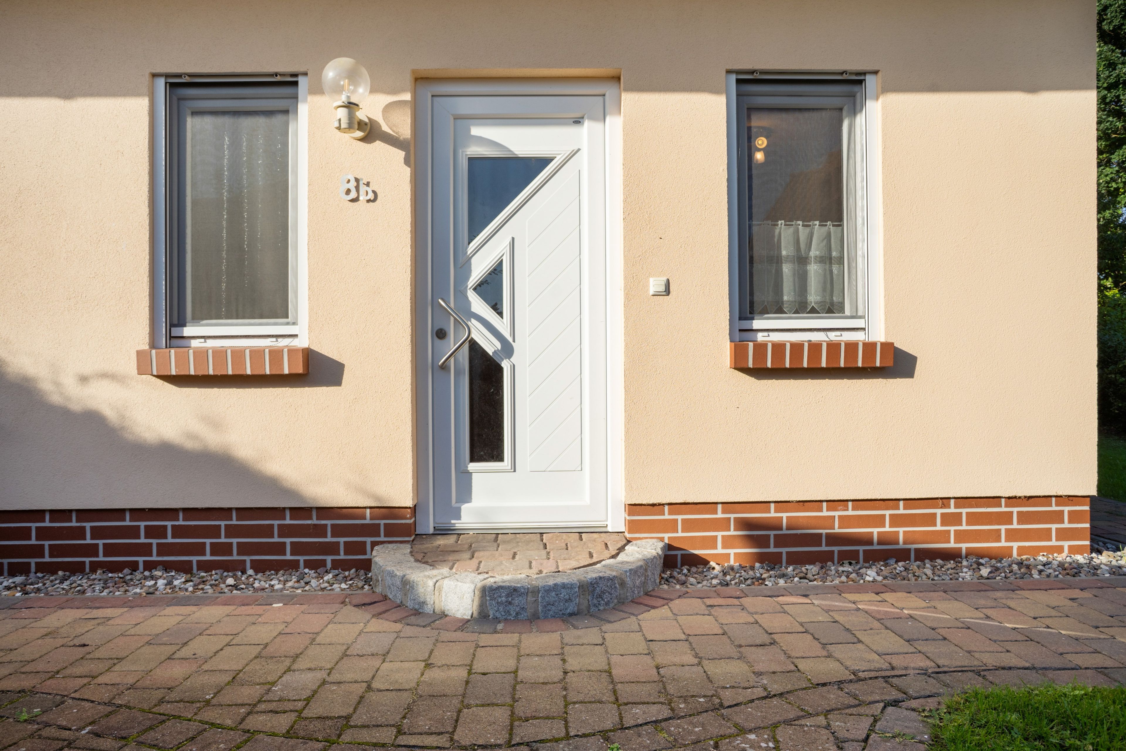 A building with a white door, two windows with shutters, and a small porch area.
