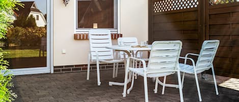 A patio with a table and chairs, a window, and a wooden fence.