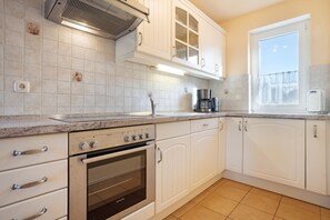 A kitchen with white cabinets, a built-in oven, a coffee maker, and a window with a view. - Hus Utblick in Fuhlendorf (Fuhlendorf)