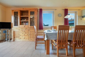 Un coin repas avec des meubles en bois, une table dressée pour deux personnes et un espace cuisine avec des placards en bois et une fenêtre.