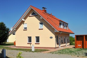 Ein zweistöckiges Haus mit rotem Ziegeldach, einem Backsteinfundament und einem kleinen angebauten Schuppen.