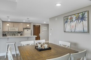 Een moderne keuken met witte kasten, een houten eettafel en een schilderij van palmbomen.