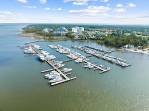 An aerial view of a marina with numerous boats docked at piers, surrounded by a coastal town with buildings and greenery. - Baytowne Wharf Village 2BR Condo - Sandestin Golf, Tennis & Marina (Miramar Beach)
