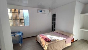 Ein Schlafzimmer mit Bett, Fenster, Klimaanlage, Tür und einem weißen Regal.