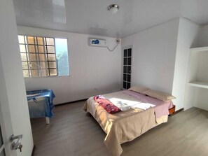 A bedroom with a bed, a window, an air conditioning unit, a door, and a white shelf. - Cozy 2-Bedroom Apartment with AC - San Cristóbal Galápagos (Galápagos Province)