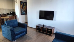 Ein Wohnzimmer mit zwei blauen Sofas, einem Fernseher und einem Bild an der Wand.