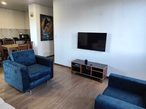 A living room with two blue sofas, a TV, and a painting on the wall. - Cozy 2-Bedroom Apartment with AC - San Cristóbal Galápagos (Galápagos Province)