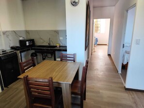 A compact kitchen with a dining table and chairs, a small stove, and a sink. - Cozy 2-Bedroom Apartment with AC - San Cristóbal Galápagos (Galápagos Province)