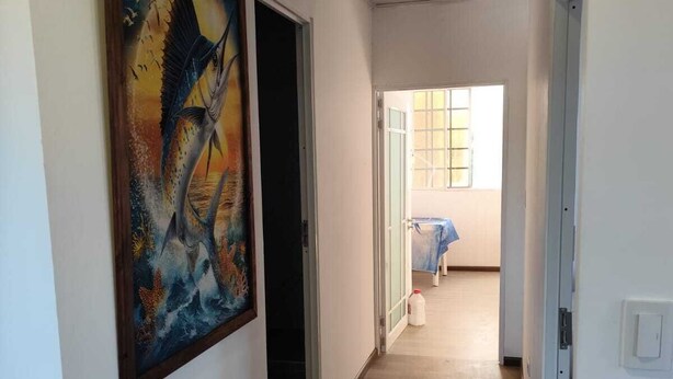Ein Flur mit Holzdielen, einem Bild an der Wand und einer offenen Tür zu einem anderen Raum.