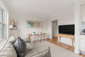 Ein modernes Wohnzimmer mit Sofa, Esstisch mit Stühlen, Flachbildfernseher und Küchenzeile.