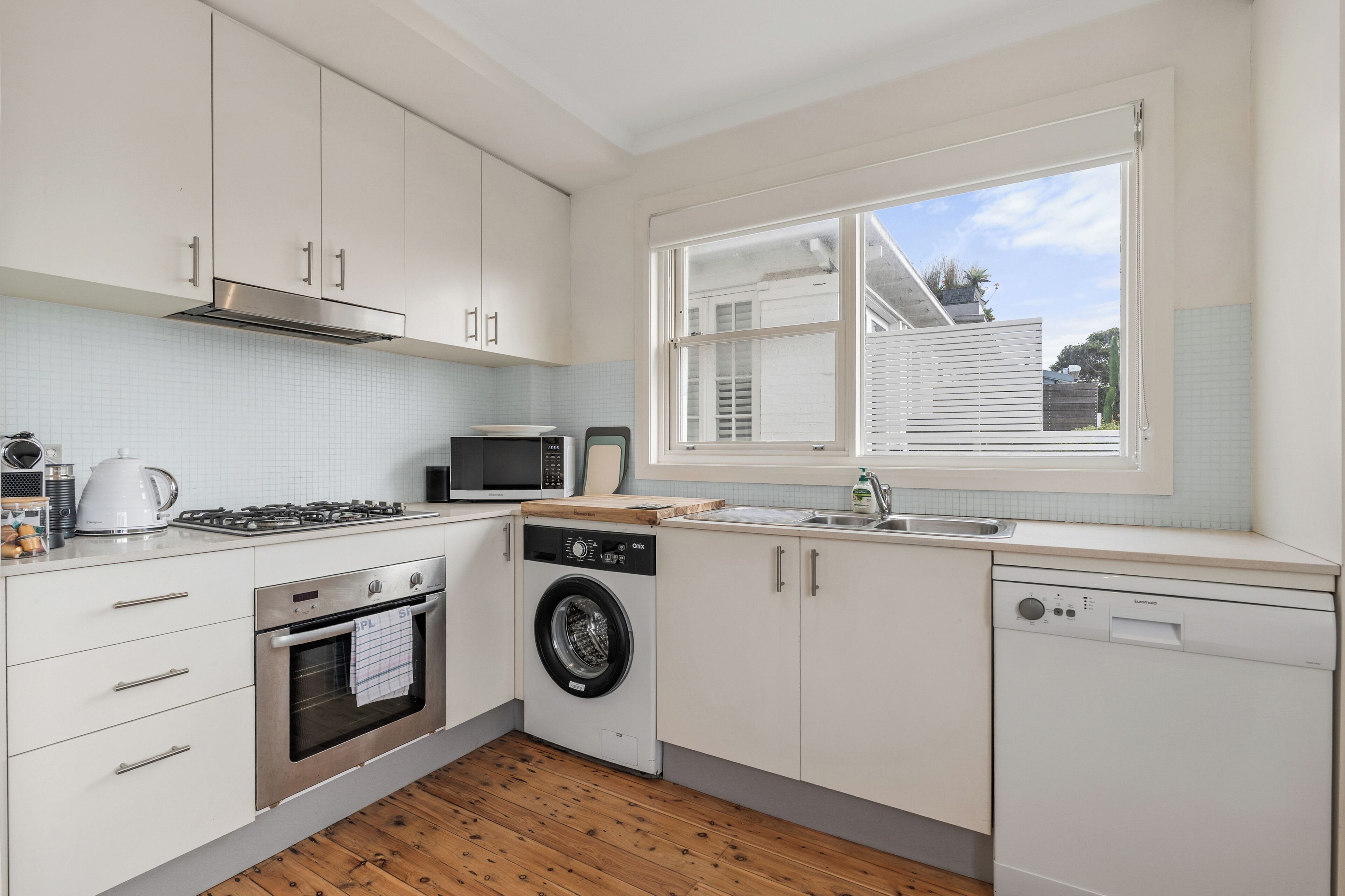 A modern kitchen with white cabinetry, a built-in oven, microwave, dishwasher, and a washing machine.