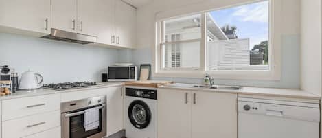 A modern kitchen with white cabinetry, a built-in oven, microwave, dishwasher, and a washing machine.