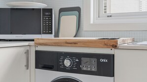 A compact kitchen with a microwave, a breadboard, and a washing machine. - Golden Sands The Best of Bondi on Your Doorstep (Bondi Beach)