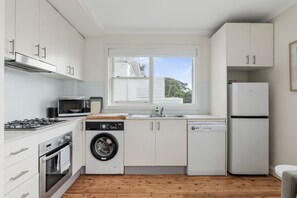 Eine kompakte Küche mit weißen Schränken, einer eingebauten Mikrowelle, einem Geschirrspüler, einem Herd und einem Kühlschrank.