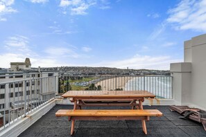 A wooden picnic table on a rooftop terrace with a view of a beach and cityscape. - Golden Sands The Best of Bondi on Your Doorstep (Bondi Beach)