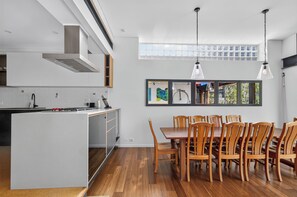 A modern kitchen with white cabinetry, a central island, and a dining area with wooden chairs and a table. - Kingsley Discover Cafs Street Art and Village Life (Newtown)