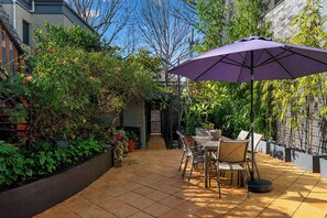 A patio with a table and chairs, surrounded by lush greenery and a purple umbrella. - Kingsley Discover Cafs Street Art and Village Life (Newtown)