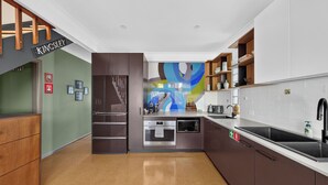 A modern kitchen with stainless steel appliances, wooden cabinets, and a colorful abstract mural on the wall. - Kingsley Discover Cafs Street Art and Village Life (Newtown)