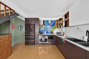 A modern kitchen with stainless steel appliances, wooden cabinets, and a colorful abstract mural on the wall. - Kingsley Discover Cafs Street Art and Village Life (Newtown)