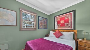 A bedroom with a bed, a nightstand, a wooden dresser, a window with a view, and three framed pictures on the wall. - Kingsley Discover Cafs Street Art and Village Life (Newtown)