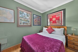A bedroom with a bed, a nightstand, a wooden dresser, a window with a view, and three framed pictures on the wall. - Kingsley Discover Cafs Street Art and Village Life (Newtown)