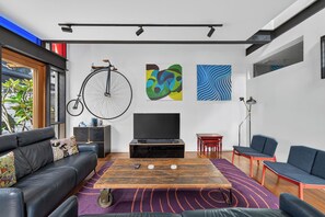 A modern living room with a sofa, a coffee table, a TV, and artwork on the wall. - Kingsley Discover Cafs Street Art and Village Life (Newtown)
