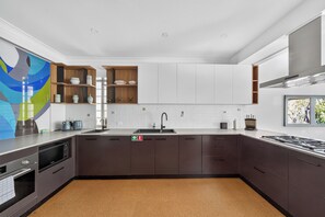 A modern kitchen with dark cabinetry, a stainless steel sink, and a built-in stove. - Kingsley Discover Cafs Street Art and Village Life (Newtown)