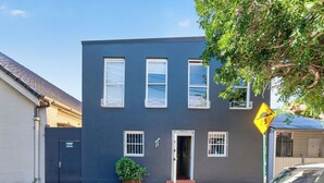 A two-story building with a dark facade, three windows on the ground floor, and a door. - Kingsley Discover Cafs Street Art and Village Life (Newtown)