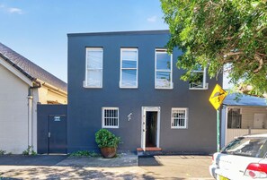 A two-story building with a dark facade, three windows on the ground floor, and a door. - Kingsley Discover Cafs Street Art and Village Life (Newtown)