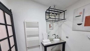 A bathroom with a white tiled floor, a black-framed mirror, a white sink, and a towel rack.