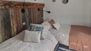 A bedroom with a wooden headboard, two beds, multiple pillows, a wall-mounted lamp, and several round mirrors.