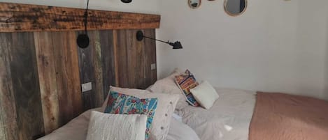 Een slaapkamer met een houten hoofdbord, twee bedden, meerdere kussens, een muurlamp en diverse ronde spiegels.