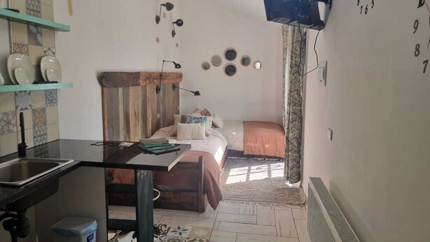 Ein kleines Zimmer mit einem Bett, einem Schreibtisch, einem kleinen Fenster und einer Wanduhr.